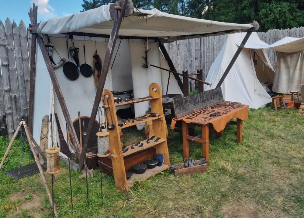 Średniowieczne stoisko kowalskie pod namiotem przy drewnianej palisadzie